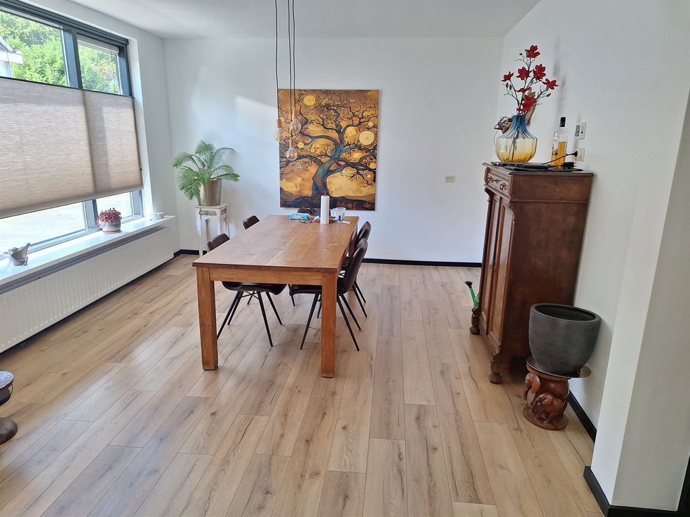 De eettafel van hout met zwarte stoelen en een groot schilderij van een boom