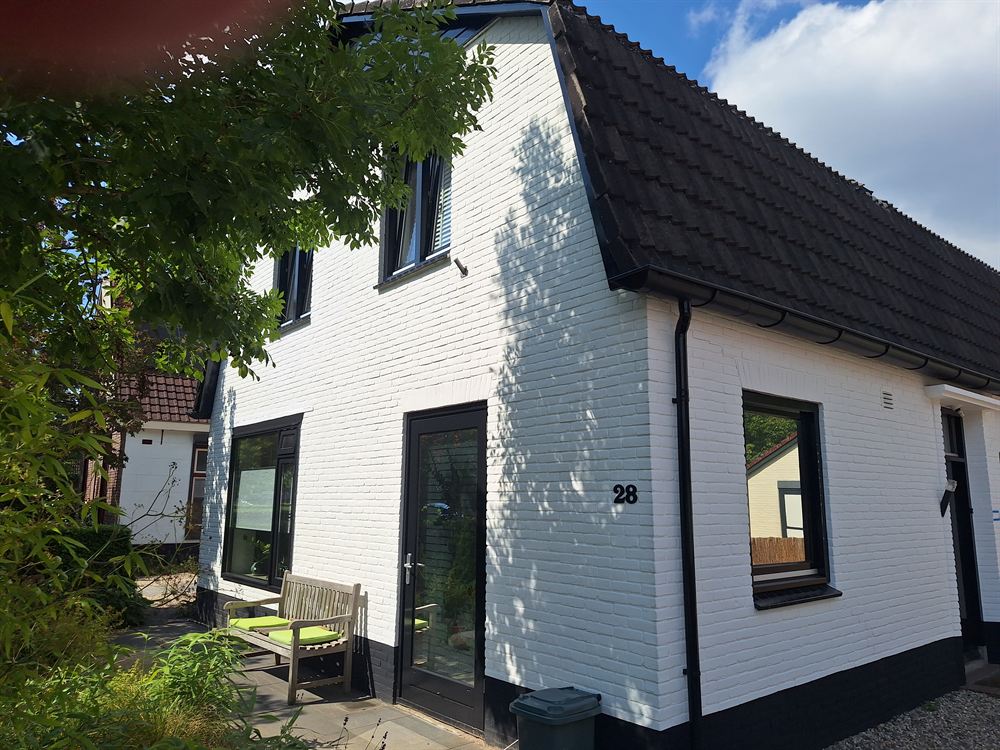 Het witte huis met terras, tuinstoelen en de heg eromheen